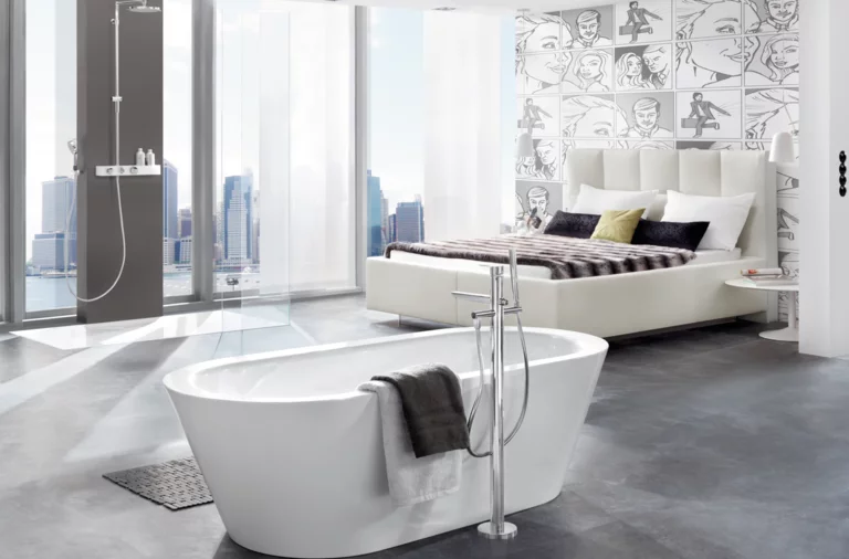 Bañera ovalada independiente de acero esmaltado con toalla, zona de ducha moderna al fondo, diseño de espacio luminoso.
